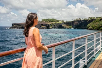 Femme en robe lin sur le pont d'un bateau de croisière contemplant les côtes volcaniques de l'île de la Réunion depuis la mer