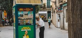 man in white dress shirt and black pants standing beside blue and yellow food stall