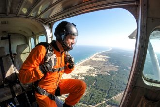Parachutiste en combinaison orange prêt à sauter depuis un avion au-dessus de Soulac-sur-Mer avec vue sur l'océan Atlantique