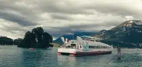 white and red passenger boat floating on body of water near island